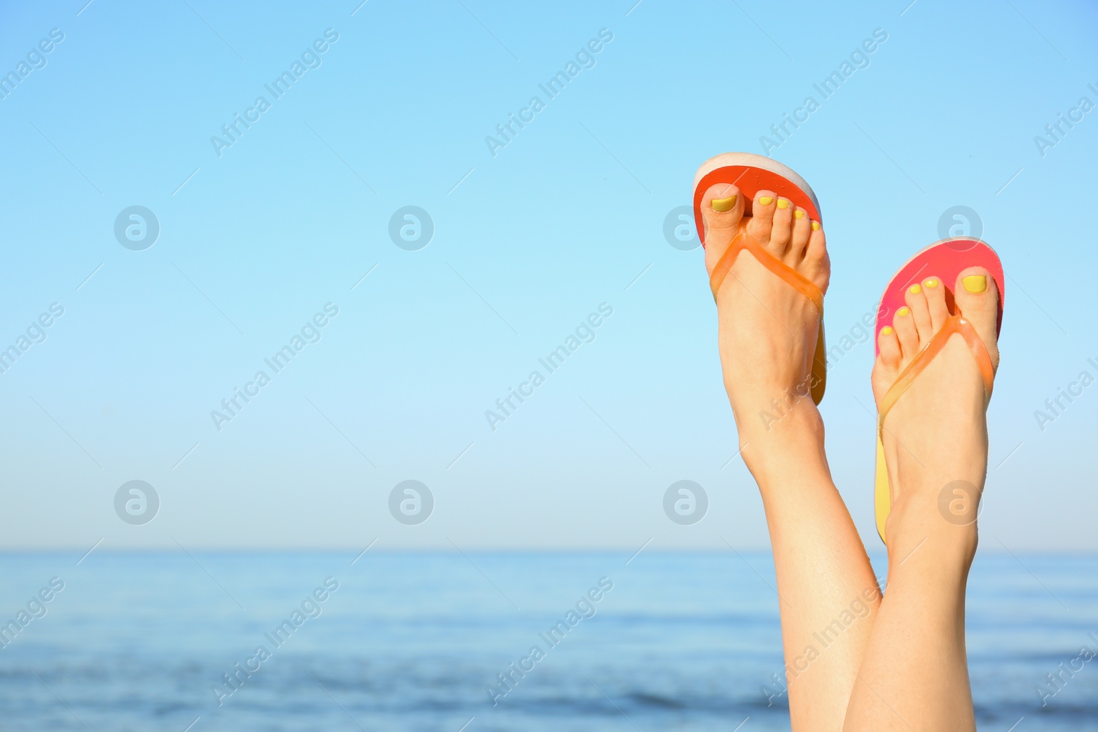 Photo of Closeup of woman wearing flip flops near sea, space for text. Beach accessories