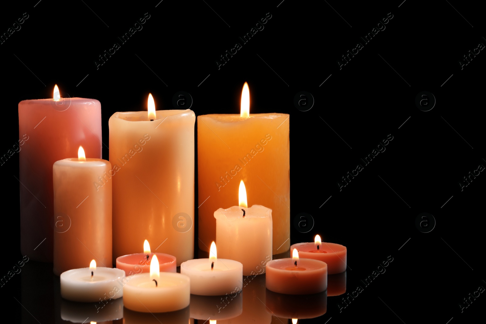 Photo of Different wax candles burning on black background