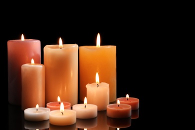 Photo of Different wax candles burning on black background