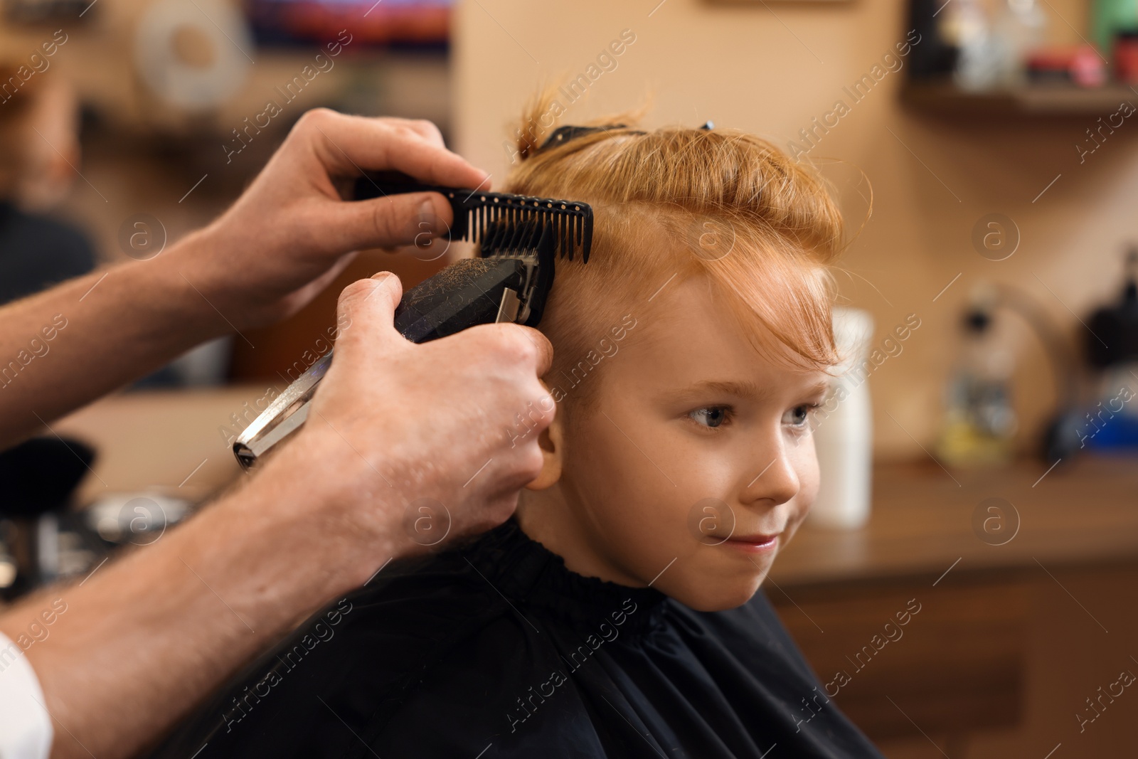 Photo of Professional hairdresser cutting boy's hair in beauty salon, closeup