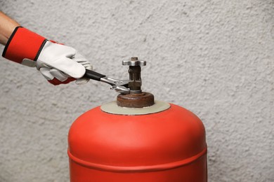 Photo of Worker with adjustable wrench opening red gas cylinder near wall, closeup