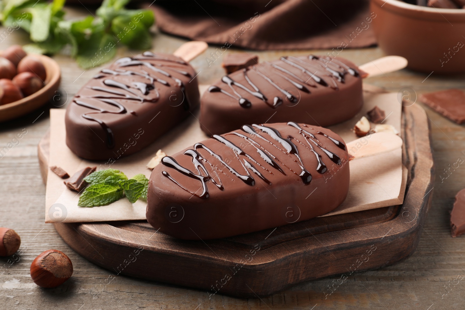 Photo of Delicious glazed ice cream bars, nuts and mint on wooden table