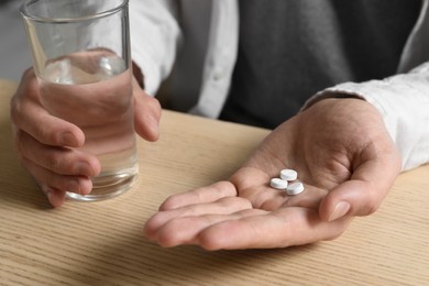 Man with glass of water and pills at wooden table, closeup