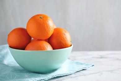 Photo of Delicious ripe tangerines in bowl on white marble table. Space for text