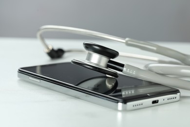 Photo of Modern smartphone and stethoscope on white table, closeup