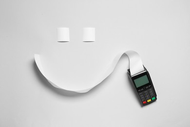 Payment terminal and smiley face made of thermal paper for receipt on light grey background, flat lay