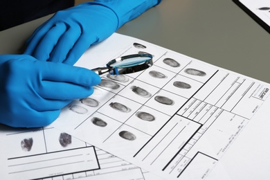 Criminalist exploring fingerprints with magnifying glass at table, closeup