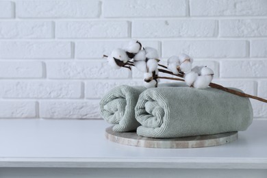 Photo of Clean towels and cotton branch with fluffy flowers on white table against brick wall, space for text