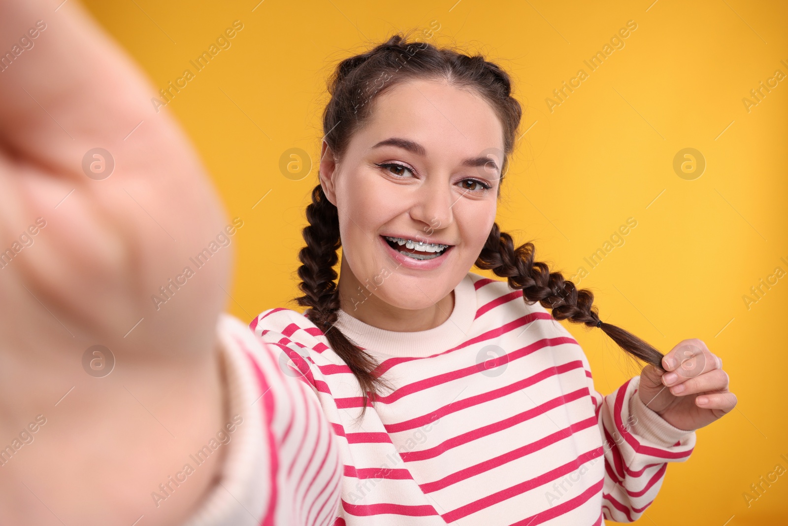 Photo of Smiling woman with braces taking selfie on orange background