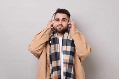 Photo of Smiling man in warm scarf listening to music on light grey background