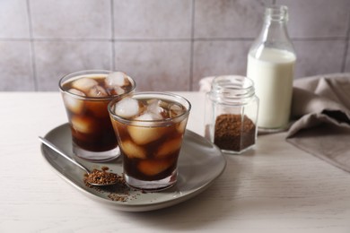 Photo of Refreshing iced coffee with milk in glasses, ingredients and spoon on light table