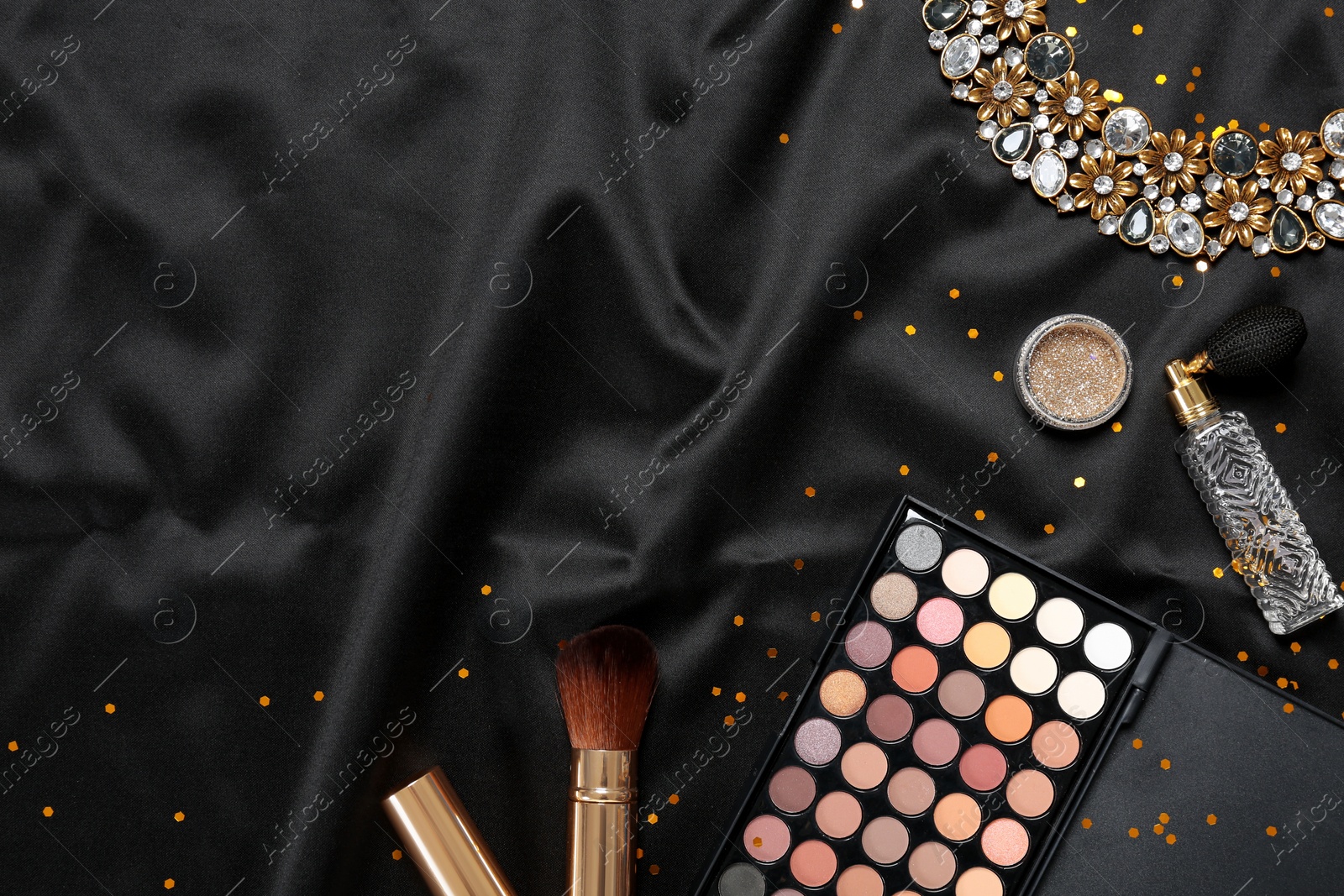 Photo of Beautiful necklace, makeup products and perfume on black fabric, flat lay. Space for text