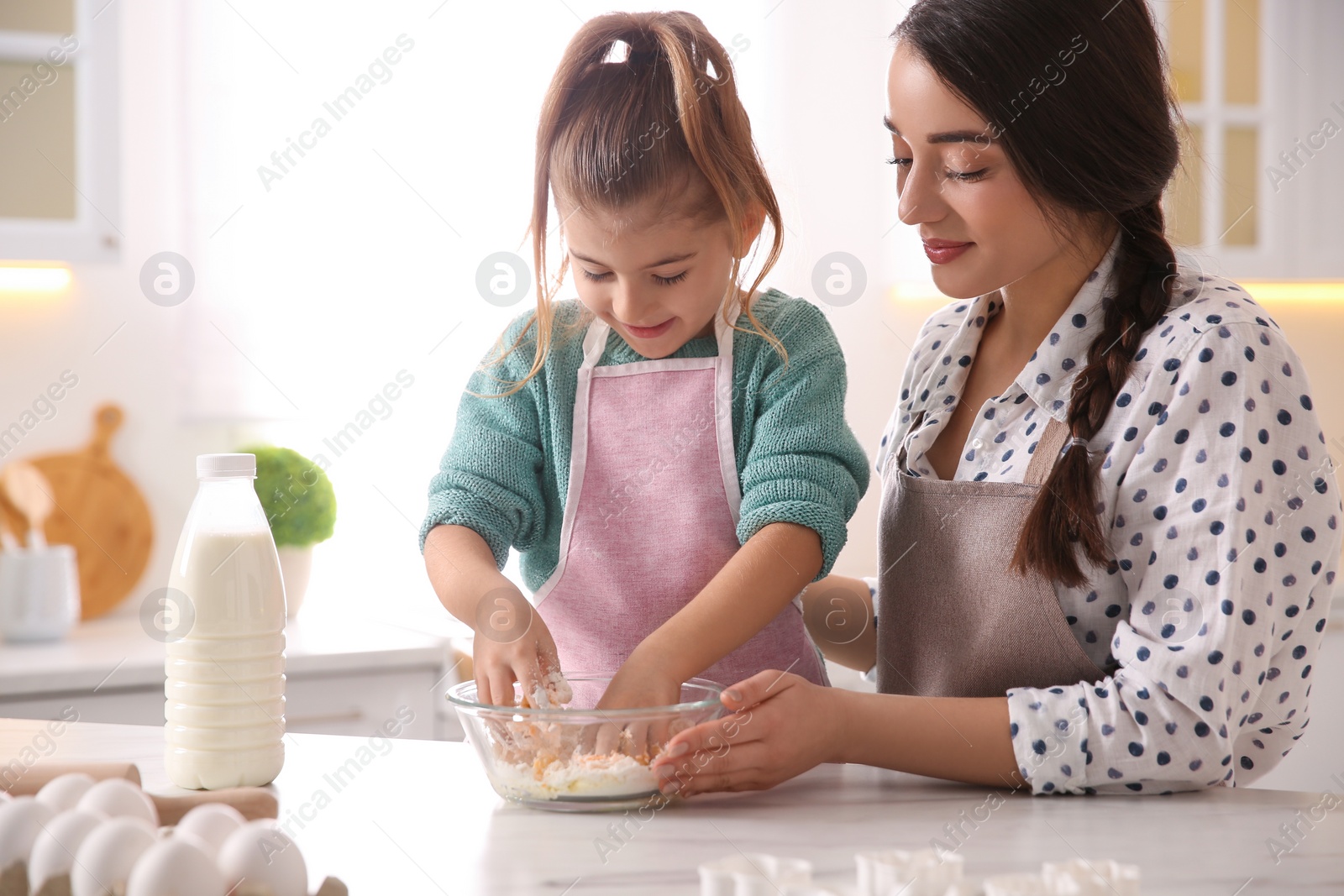 Photo of Mother and daughter making dough at table in kitchen