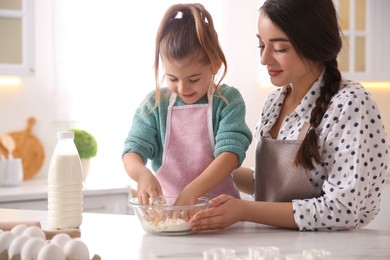 Photo of Mother and daughter making dough at table in kitchen