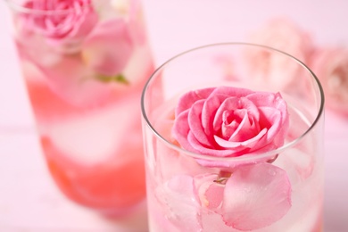 Photo of Delicious refreshing drink with lemon and roses on pink wooden table, closeup