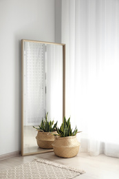 Photo of Large mirror with wooden frame near window in light room