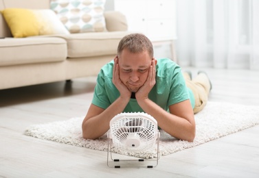 Young man suffering from heat in front of small fan at home