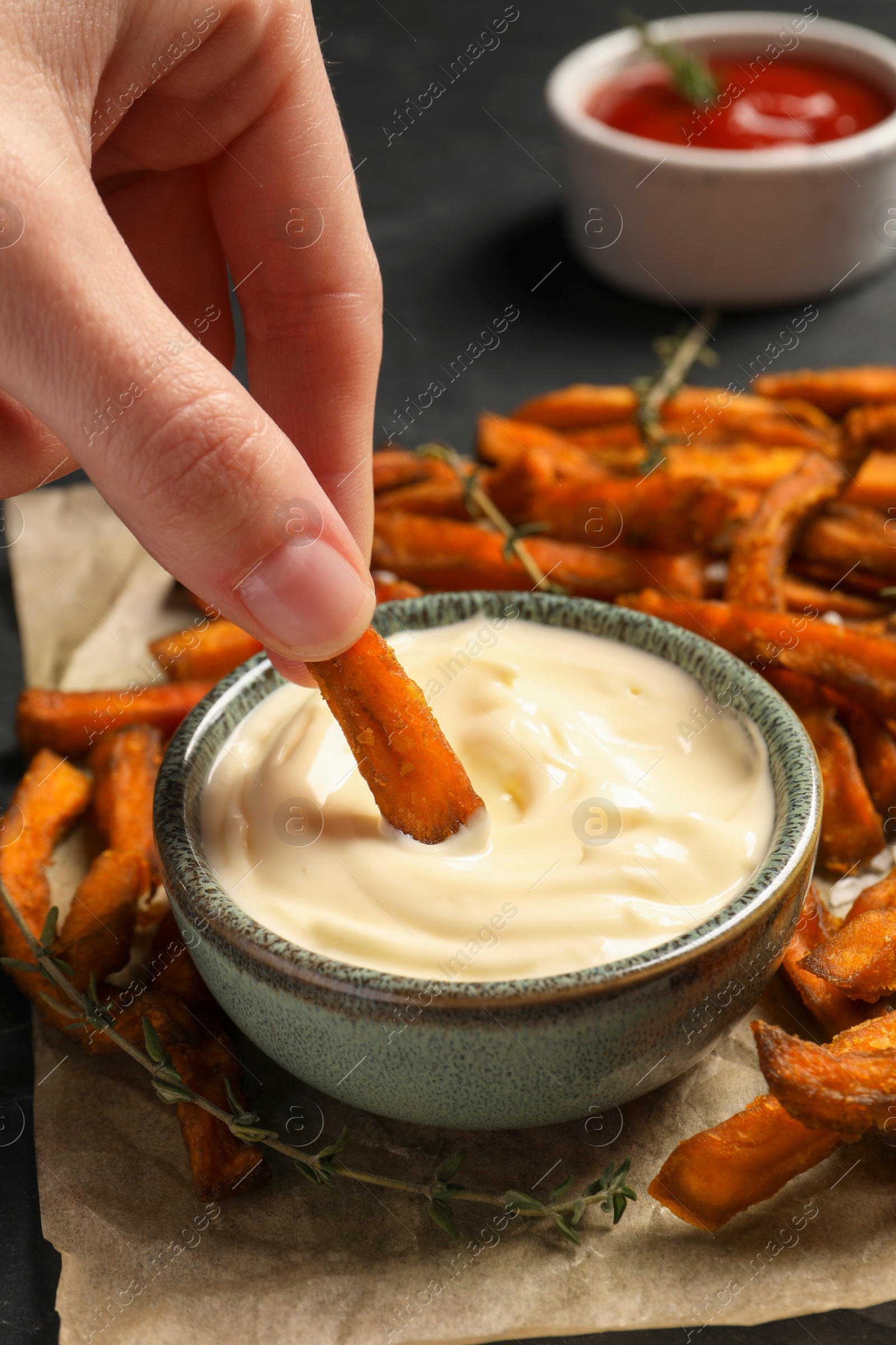 Photo of Woman dipping sweet potato fries into sauce at table, closeup