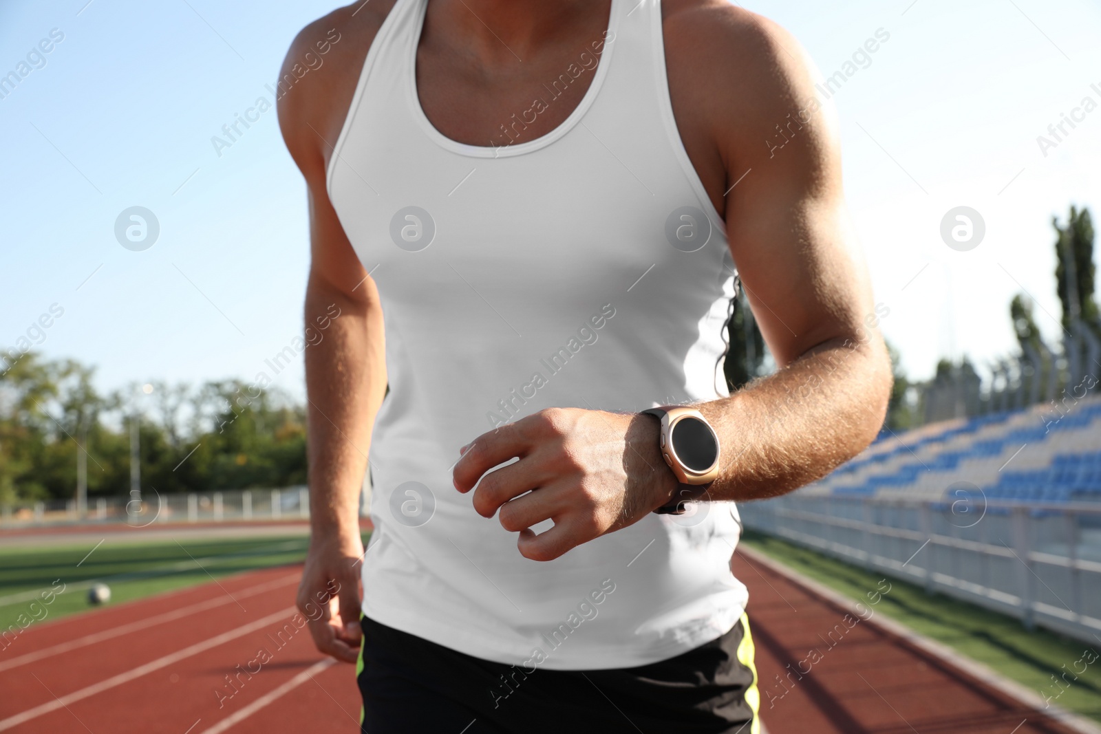 Photo of Man with fitness tracker running at stadium, closeup