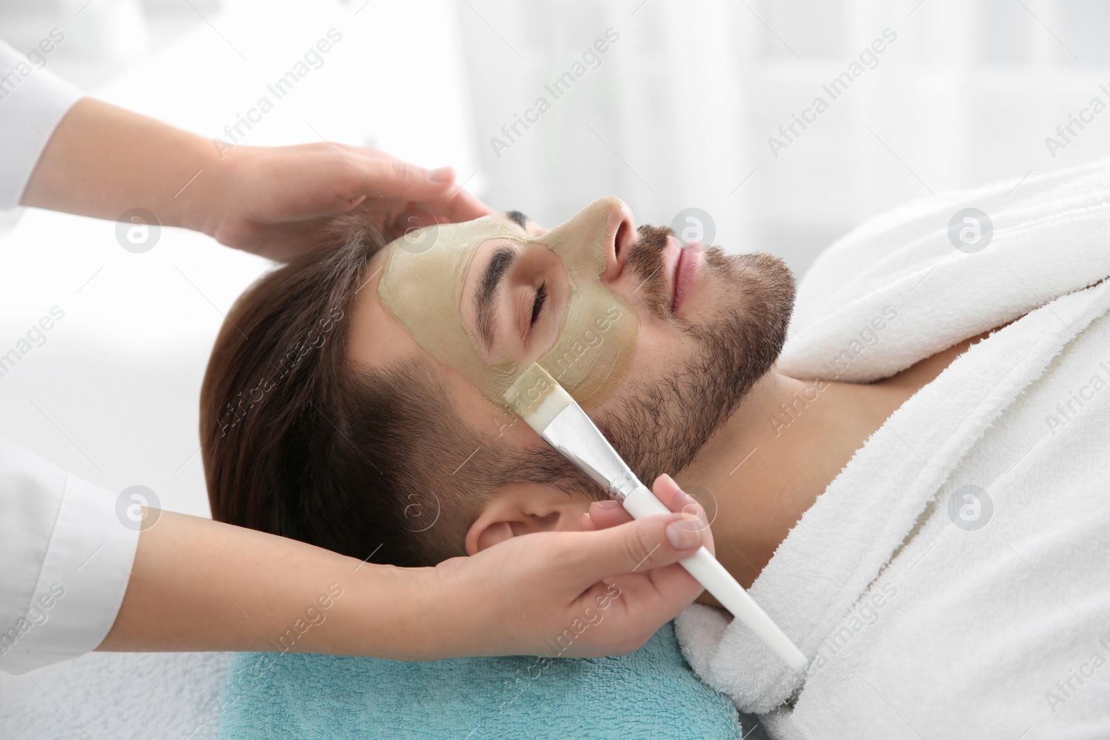 Photo of Cosmetologist applying mask on client's face in spa salon