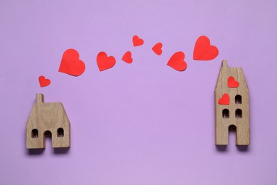 Photo of Paper hearts between two wooden house models on violet background symbolizing connection in long-distance relationship, flat lay