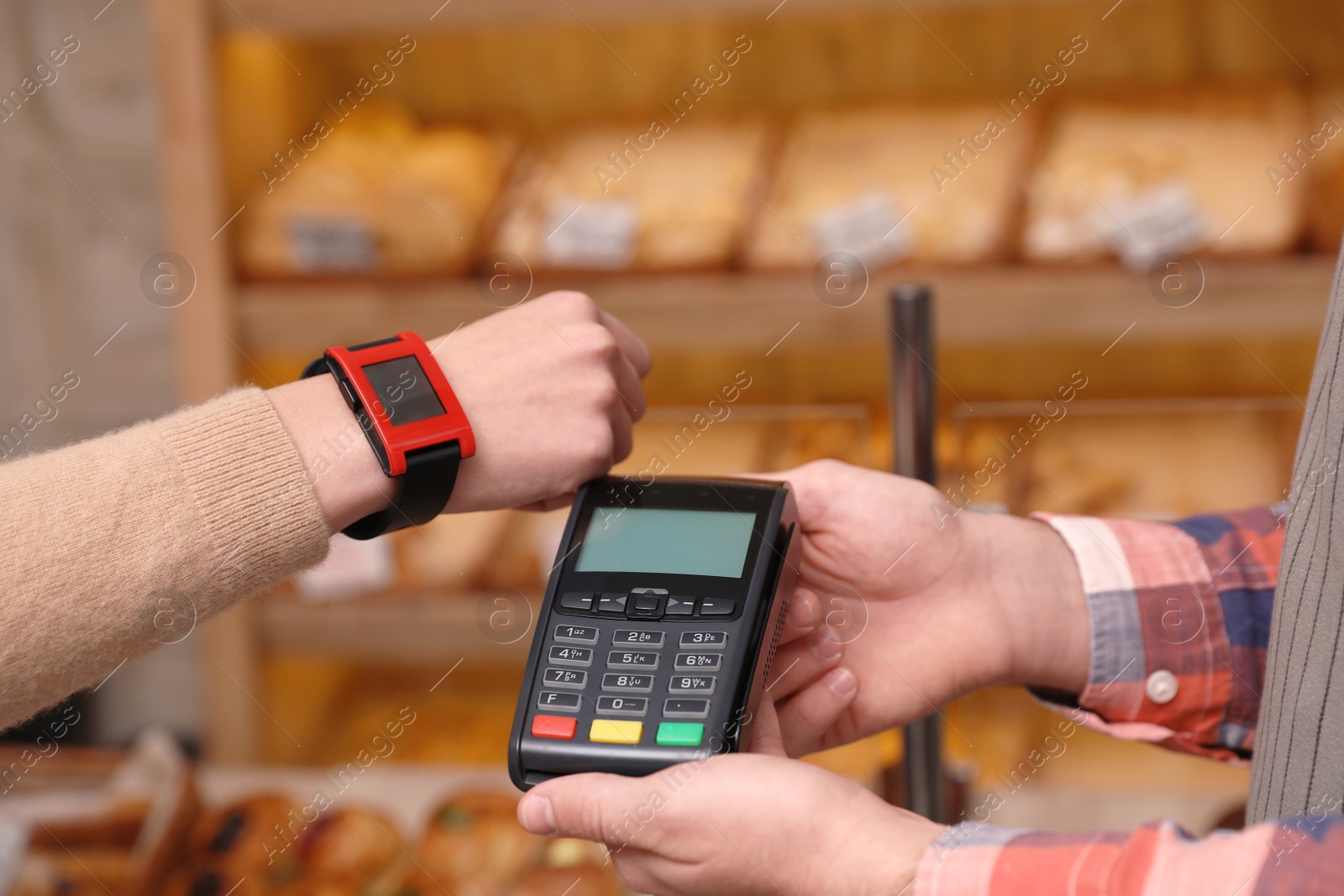 Photo of Woman using terminal for contactless payment with smartwatch in bakery, closeup