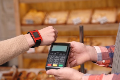 Photo of Woman using terminal for contactless payment with smartwatch in bakery, closeup
