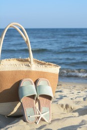 Photo of Straw bag, slippers and dry starfish on sandy beach near sea
