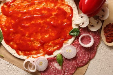 Photo of Pizza base smeared with tomato sauce and products on light textured table, top view