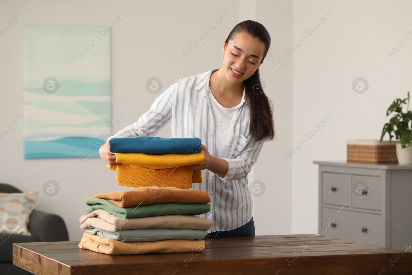 Photo of Young woman folding clothes at wooden table indoors