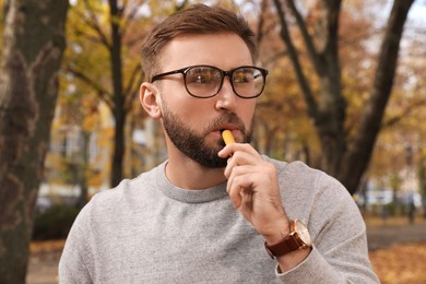 Photo of Handsome young man using disposable electronic cigarette in park on autumn day