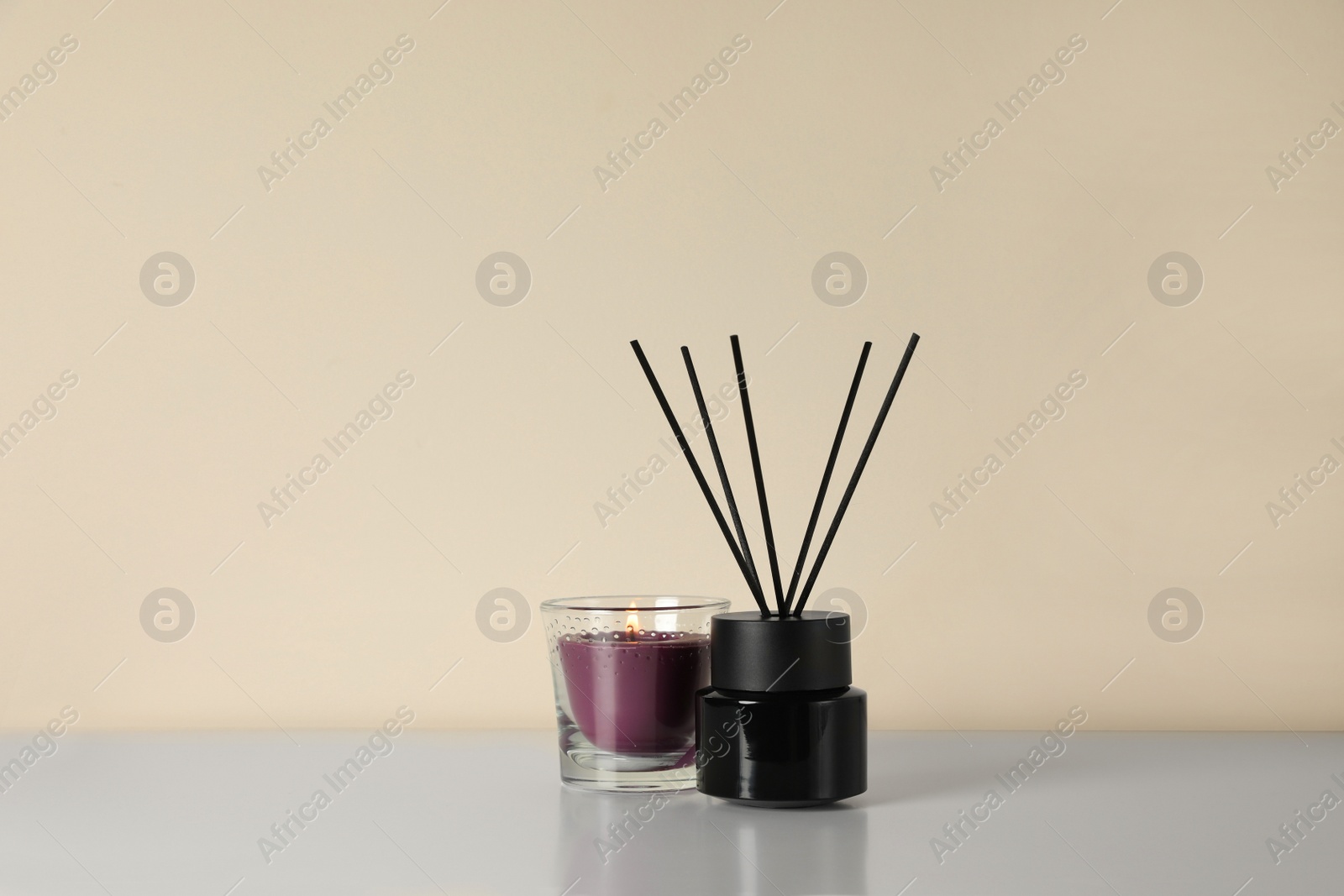 Photo of Aromatic reed air freshener and candle on white table indoors