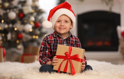 Photo of Cute little boy holding gift box in room decorated for Christmas