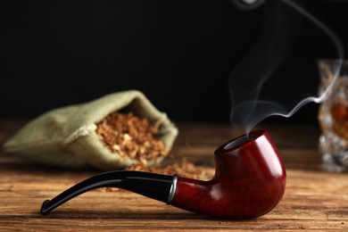Photo of Stylish tobacco pipe with smoke on wooden table