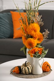 Beautiful bouquets with bright orange flowers and pumpkins on coffee table indoors. Autumn vibes