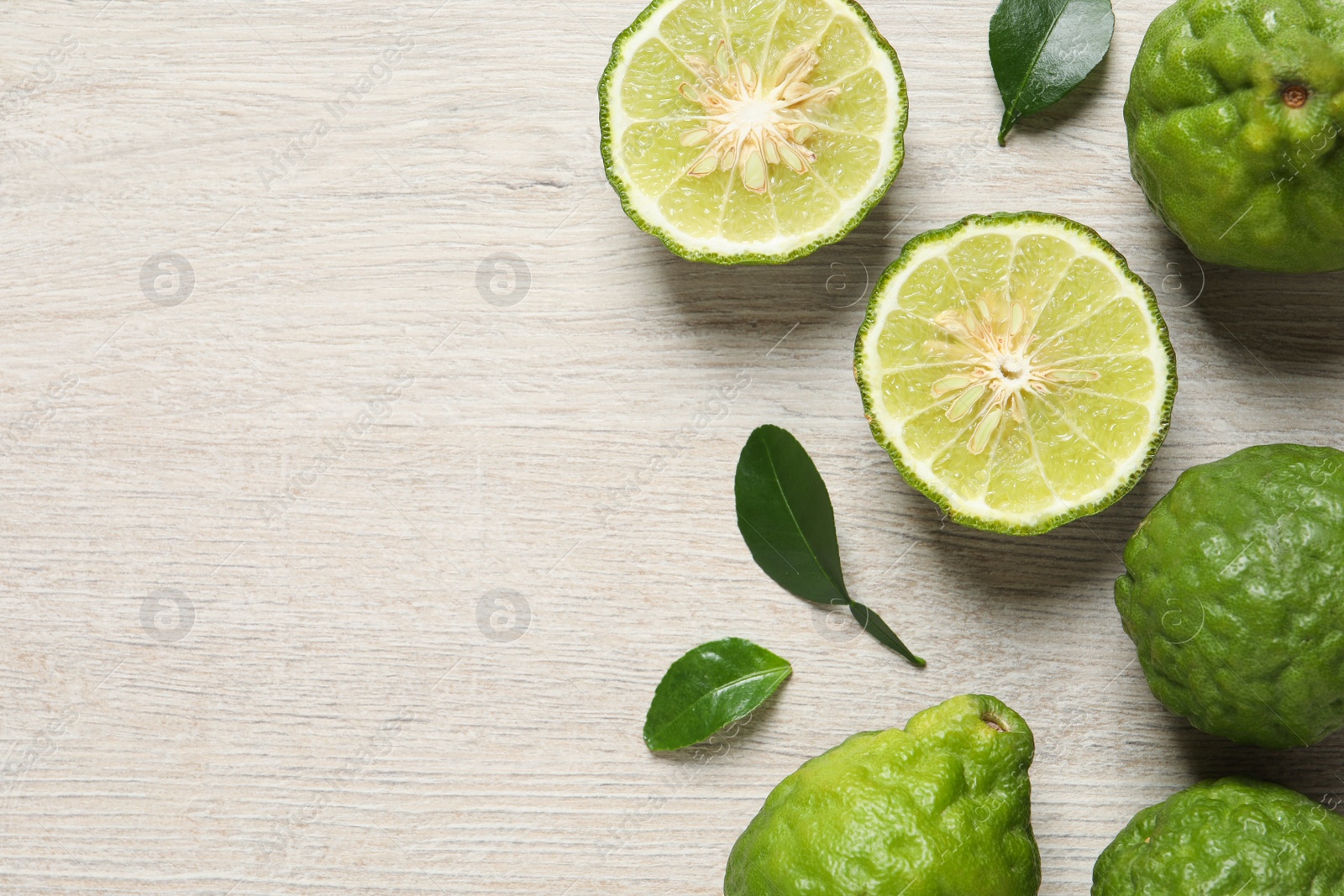 Photo of Whole and cut ripe bergamot fruits with green leaves on white wooden table, flat lay. Space for text