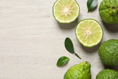 Whole and cut ripe bergamot fruits with green leaves on white wooden table, flat lay. Space for text