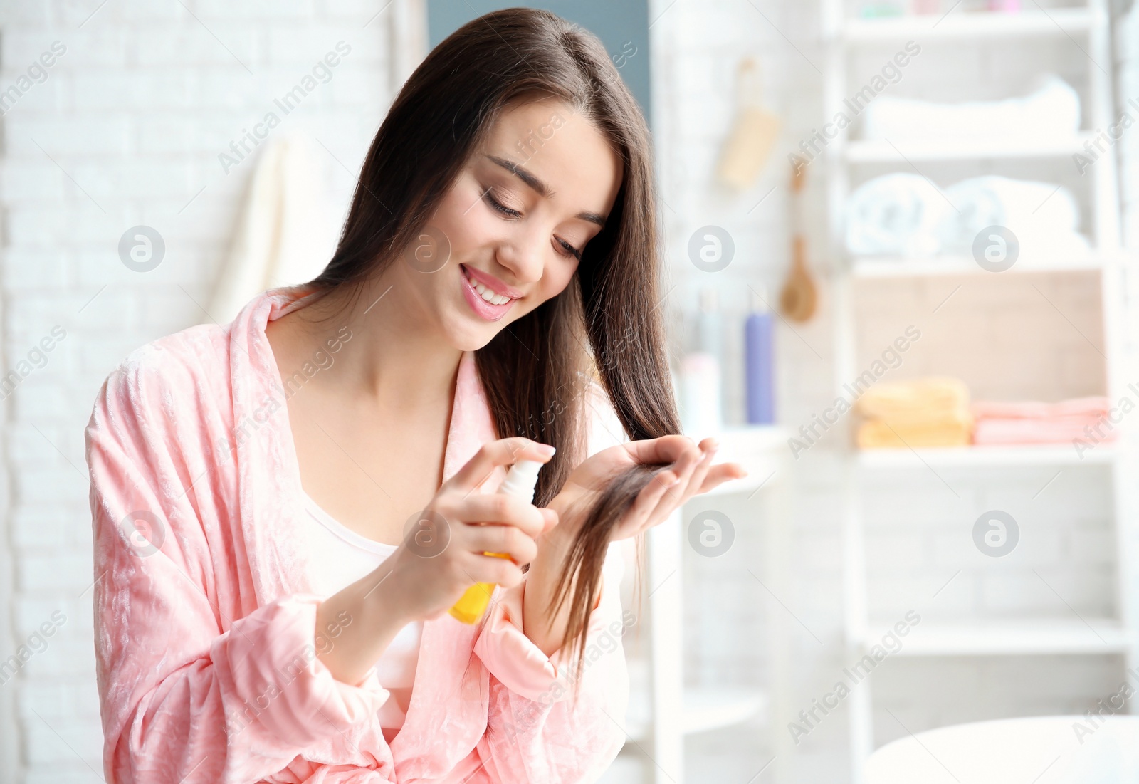 Photo of Young woman applying oil onto hair in bathroom