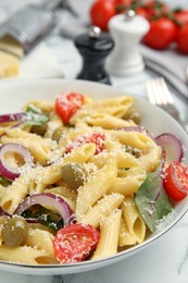 Bowl of delicious pasta with tomatoes, olives and onion on white marble table, closeup