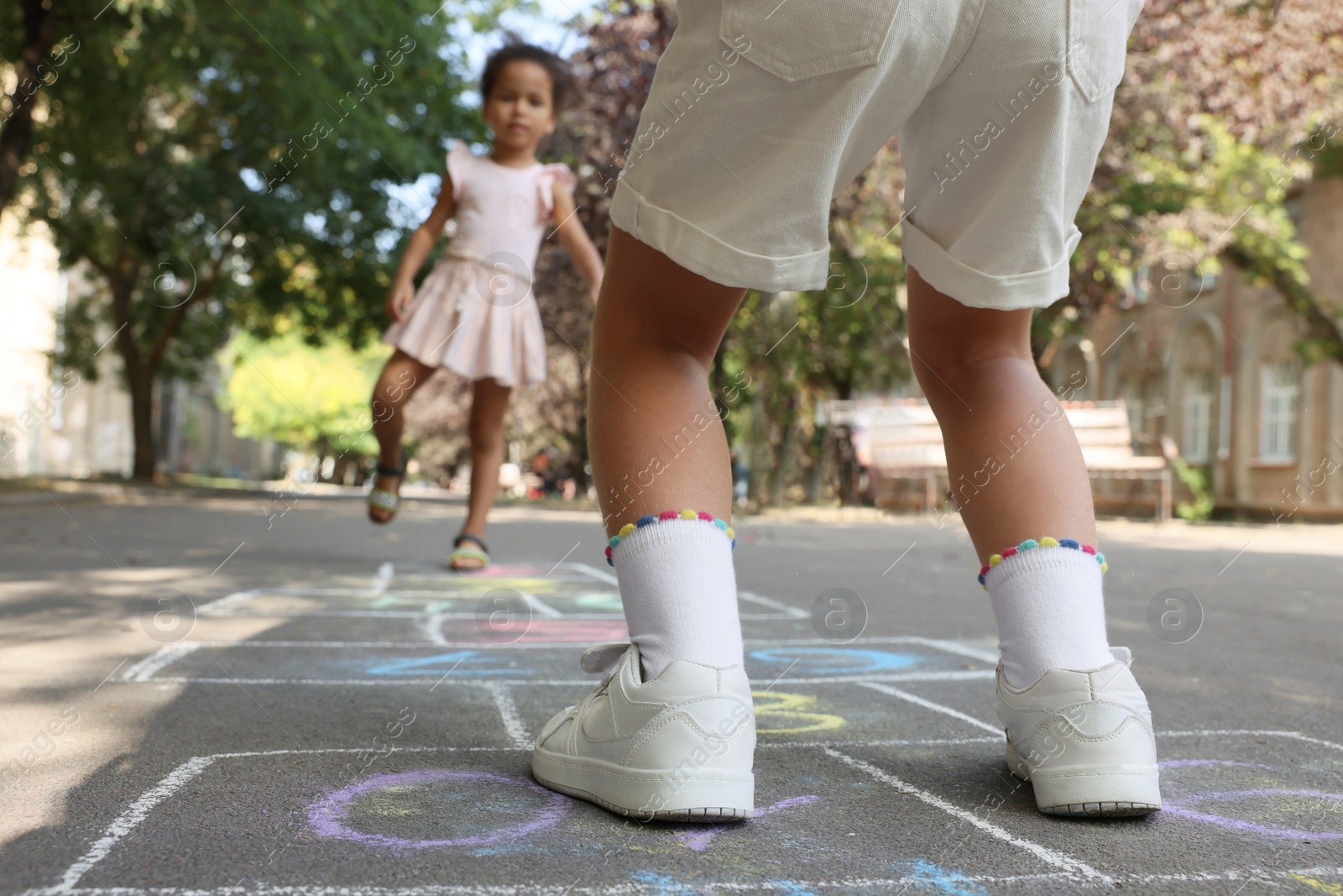 Photo of Little children playing hopscotch drawn with chalk on asphalt outdoors, closeup