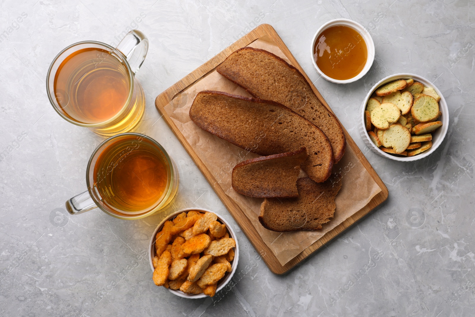Photo of Different crispy rusks, beer and dip sauce on light marble table, flat lay