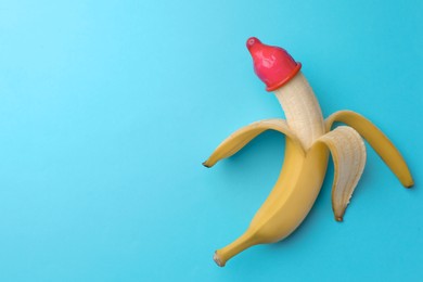 Photo of Banana with condom on light blue background, top view and space for text. Safe sex concept