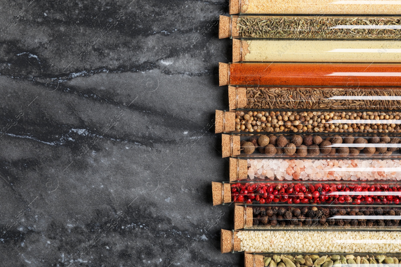 Photo of Glass tubes with different spices on grey marble table, flat lay. Space for text