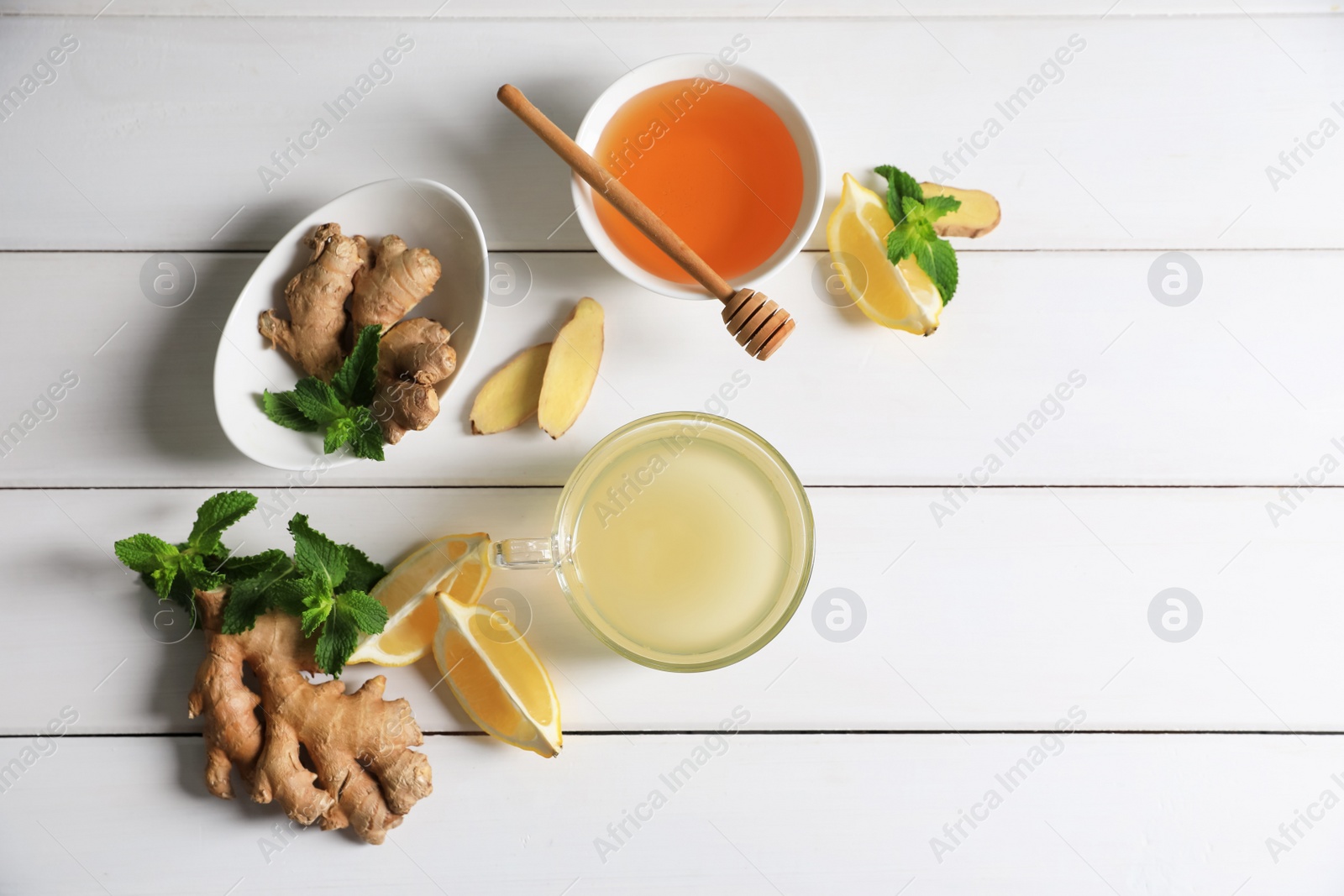 Photo of Delicious ginger tea and ingredients on white wooden table, flat lay. Space for text