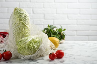 Fresh Chinese cabbages and other vegetables on white marble table near brick wall. Space for text