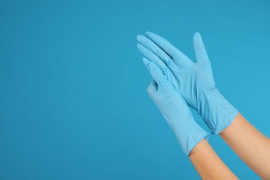 Photo of Doctor wearing medical gloves on light blue background, closeup. Space for text