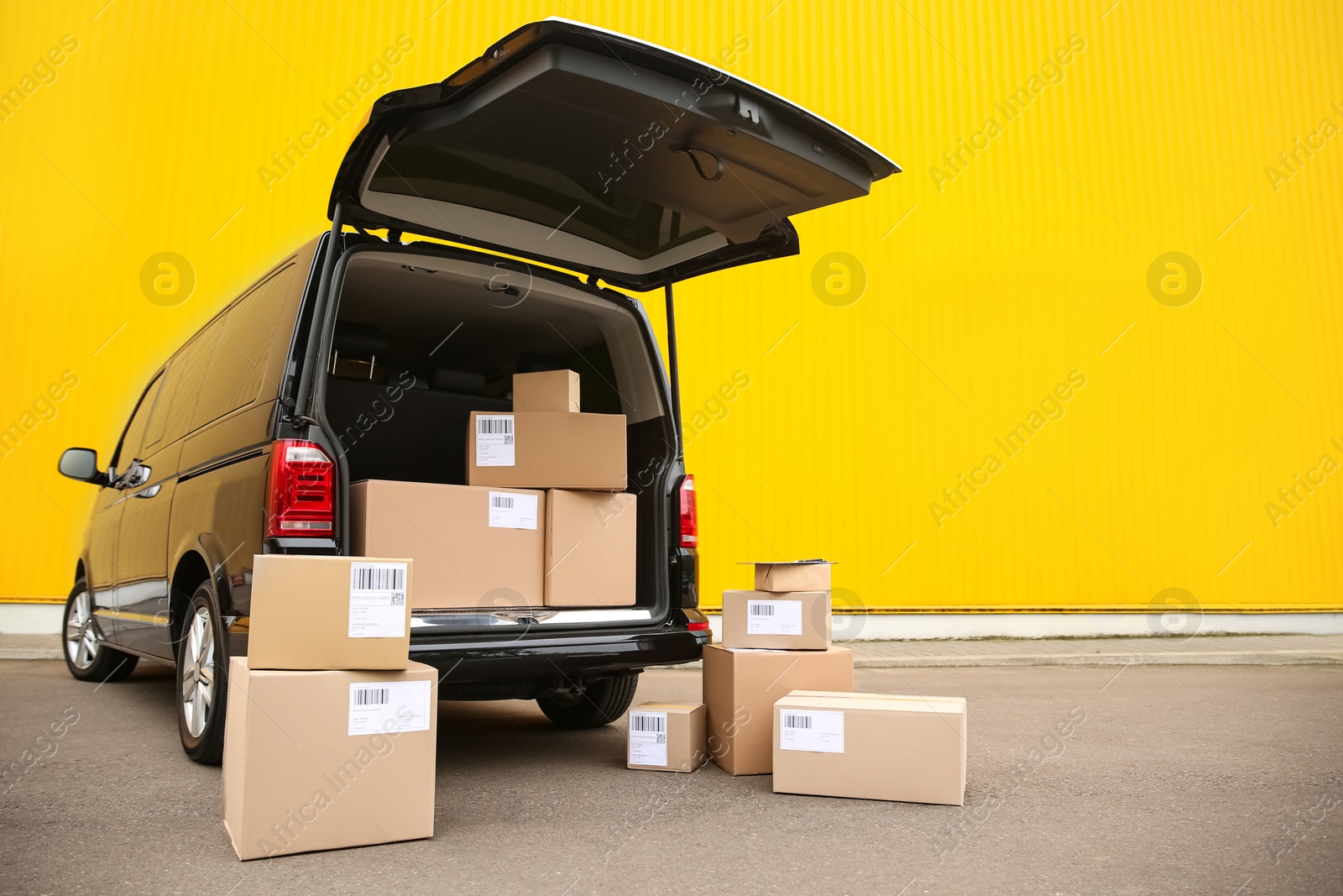 Photo of Black delivery van and many different parcels near yellow wall outdoors, space for text. Courier service