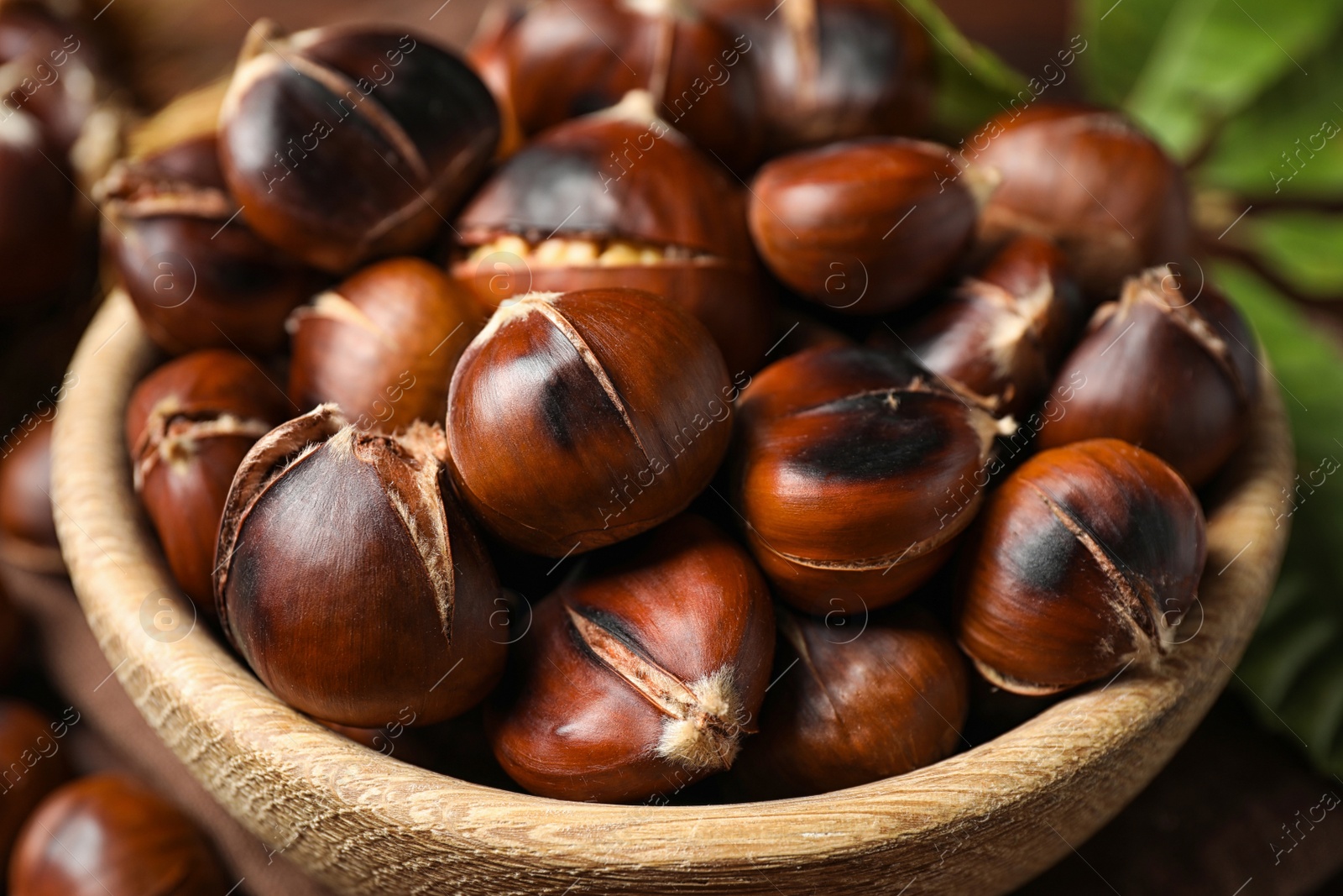 Photo of Delicious roasted edible chestnuts in wooden bowl, closeup