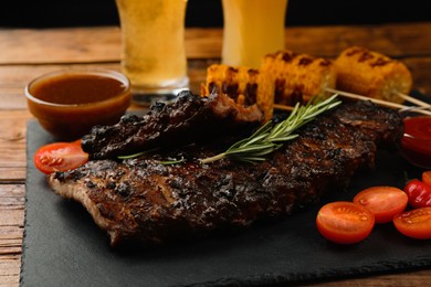 Glasses of beer, tasty fried ribs, grilled corn and sauce on wooden table, closeup