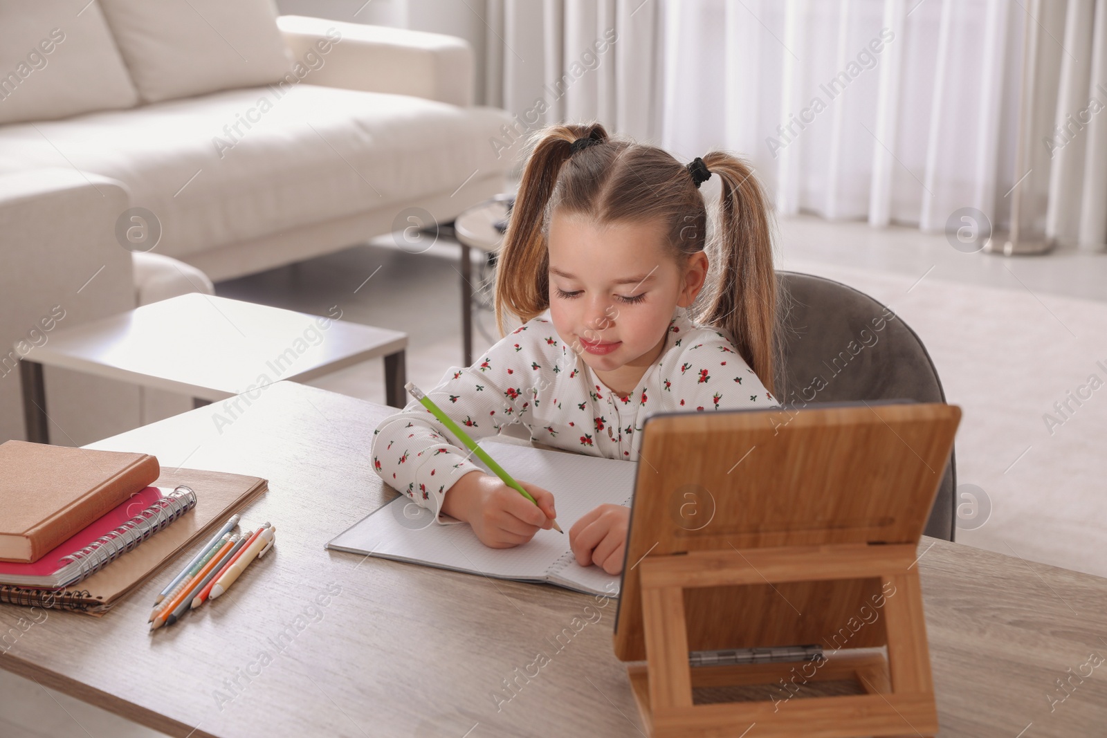 Photo of Cute little girl doing homework with tablet at home